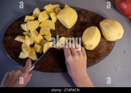 Schneiden Sie Kartoffeln mit einem Messer auf einem Schneidebrett in kleine Stücke. Abwicklung Stockfoto