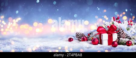 Geschenkbox Auf Schnee Mit Bokeh-Lichtern Und Ornament In Tannenzweig - Frohe Weihnachten Stockfoto