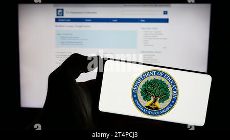 Person, die vor der Webseite ein Handy mit dem Siegel des US-Bildungsministeriums hält. Schwerpunkt auf dem Display des Telefons. Stockfoto