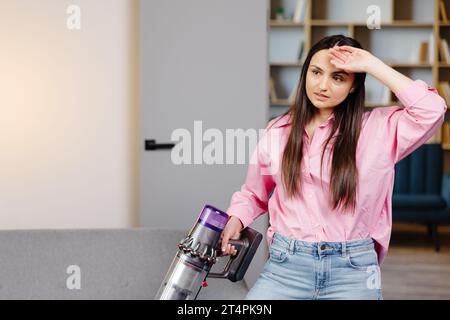 Müde und erschöpfte Frau, die das Haus saugt, Teppich im Wohnzimmer putzt, frustriert, viel Arbeit am Haus zu machen, um sich eine Minute lang auszuruhen Stockfoto