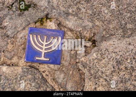 Kleine blaue Fliese mit Menorahsymbol, eingebettet in den Pflaster des ehemaligen jüdischen Viertels Toledo, Spanien, Kopierraum. Stockfoto