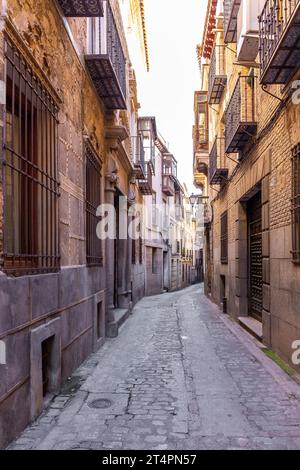Enge spanische mittelalterliche Kopfsteinpflasterstraße mit alten Wohnhäusern, traditionellen geschmiedeten Balkonen und Straßenlaternen im alten Stil, Toledo, Spanien. Stockfoto