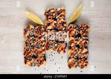 Set gebackener Sushi-Brötchen, bestreut mit Sesamsamen auf weißem Holzhintergrund. Stockfoto