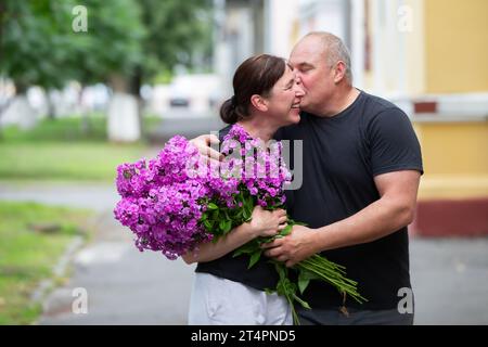 Ein glückliches älteres Paar mit einem Blumenstrauß spaziert durch die Sommerstadt. Stockfoto