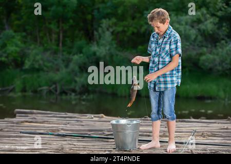 Ein Fischerjunge steht auf einer hölzernen Brücke und schaut den gefangenen Karpfen an. Stockfoto