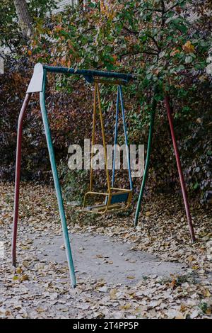 Alte Schaukel auf einem Kinderspielplatz aus Metall. Sowjetischer Hof im Herbstlaub. Veraltete unsichere Spielelemente Stockfoto