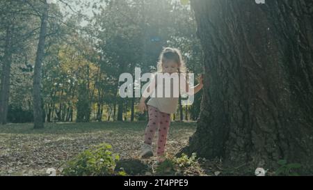 Blick auf ein kleines Mädchen in lässiger Kleidung, das allein im Herbstpark spaziert und die Natur erkundet. Das junge weiße kleine Mädchen. Herbstferien auf der Natur. Stockfoto