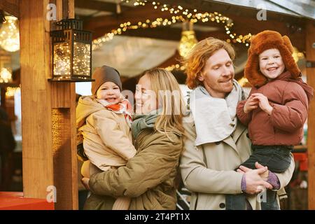 Außenporträt einer glücklichen jungen Familie auf dem Weihnachtsmarkt, Eltern mit 2 kleinen Kindern genießen Urlaub, reisen mit Kindern Stockfoto