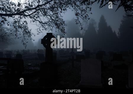 Gruselige Grabsteine auf einem Friedhof in einer nebligen, geheimnisvollen Nacht im Winter. Stockfoto