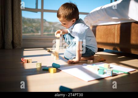 Kleiner Junge baut einen Turm mit Holzblöcken. Entzückendes kaukasisches Kind, das Spielzeug stapelt und dabei die Feinmotorik und Hand-Augen-Koordination fördert Stockfoto