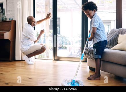 Reifer afroamerikanischer Vater und sein kleiner Sohn machen Hausarbeit in der Lounge zu Hause. Ein Schwarzer und sein Junge haben Spaß beim Putzen ihres Hauses Stockfoto