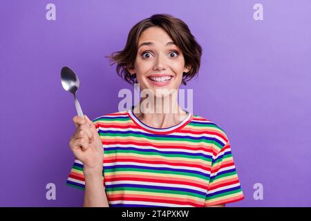 Foto von funky fröhlichem Mädchen gekleidete trendige Kleidung zeigt Löffel, der Abendessen auf lila Hintergrund isoliert will Stockfoto