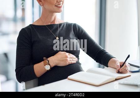 Eine Liste von Aufgaben zusammenzustellen, die ihr Ersatz folgen soll. Nahaufnahme einer schwangeren Geschäftsfrau, die in einem Büro Notizen schreibt. Stockfoto