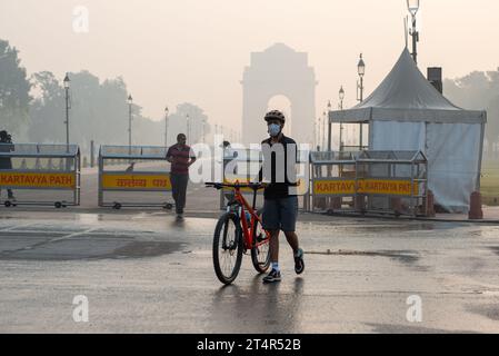 Ein Radfahrer, der eine Maske trägt, die man am India Gate während eines Smoggy frühen morgens gesehen hat. Die Luftverschmutzung in Delhi ist in erster Linie auf Fahrzeuge, Industrien, Baustaub, Abfallverbrennung und Verbrennung von Erntegutrückständen zurückzuführen. Im Winter verschärfen Temperaturumkehrungen das Problem, indem Schadstoffe in Bodennähe eingeschlossen werden. Stockfoto