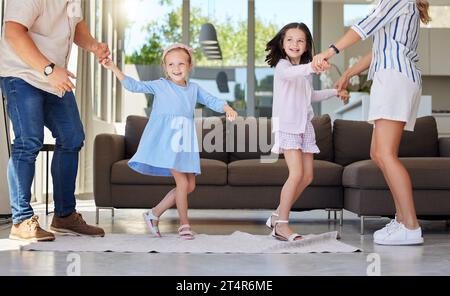 Begeisterte, glückliche Kinder, die Spaß mit energiegeladenen jungen Eltern zu Hause haben. Schwestern tanzen zusammen mit Mom und Dad. Die Familie hat Spaß beim Tanzen zu Musik Stockfoto