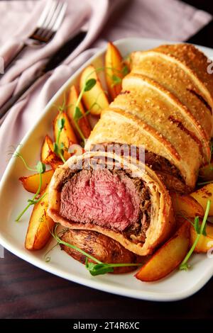 Köstliches Rindfleisch wellington serviert mit gebackenen Kartoffeln und Mikrogrün. Klassisches Steakgericht, großartiges Herzstück für besondere Anlässe. Stockfoto