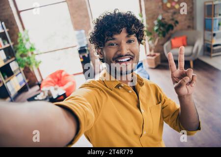 Foto-Porträt von jungen männlichen tragen gelbes Hemd Selfie Foto zeigt V-Zeichen innen Loft Industriestil Stockfoto