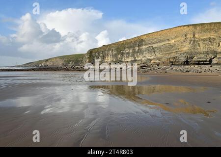 Nasser Sand führt nach Westen in Richtung der Klippen an der Dunraven Bay bei hellem Sonnenschein mit blauem Himmel und weißen Wolken und klaren Reflexen der Klippen Stockfoto