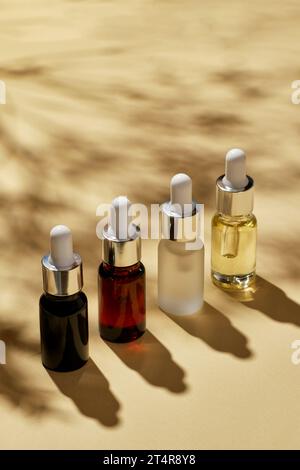 Öle zur Kurbehandlung in verschiedenen Glasflaschen auf beigem Hintergrund mit Schatten von Blättern. Kopierbereich für Text. Stockfoto