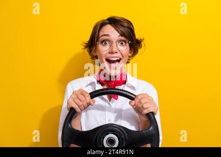 Foto von aufgeregtem fröhlichem Mädchen tragen trendiges Outfit halten Lenkrad fahren eigenes Auto Wochenendausflug isoliert auf gelbem Hintergrund Stockfoto