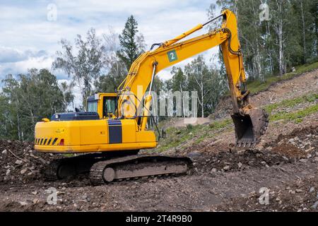 Ein gelber Bagger arbeitet in den Bergen. Straßenbau Stockfoto