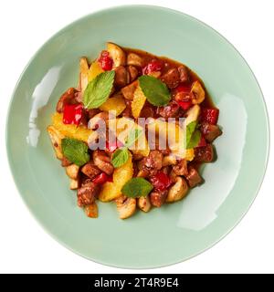 Kalbseintopf mit Paprika, Pilzen, Zwiebeln, Orangen, dekoriert mit Minzblättern, isoliert auf weißem Hintergrund. Stockfoto