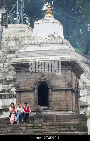 Kathmandu, Nepal: hindu-Mädchen auf der Treppe eines Minitempels am Ufer des heiligen Bagmati-Flusses, Einäscherungszeremonie im Pashupatinath-Tempel Stockfoto