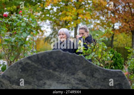 Nahaufnahme von Mutter und Tochter, die am Grab des Mannes auf dem Friedhof stehen, die Mutter blickt in die Ferne, die Tochter wischt sich die Nase, auf A Stockfoto
