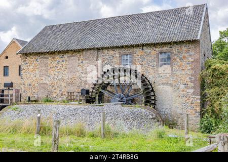 Altes Steingebäude mit Giebeldach, EPER oder Wingbergermolen Wassermühle am Fluss Geul, zwei Fenster, Bäume und wilde Vegetation im Hintergrund, bewölkt da Stockfoto