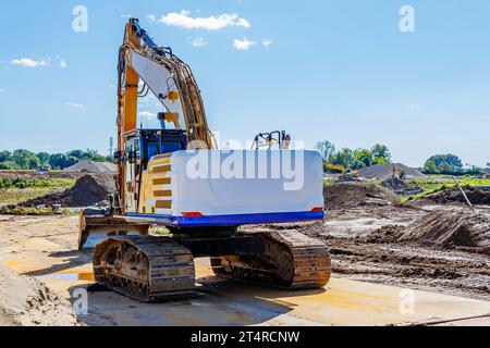 Rückansicht eines Raupenbaggers auf Arbeitsflächen im Landstraßenbau, Arbeitsmaschinen, Industrieland und Bäume vor blauem Himmel im Ba Stockfoto