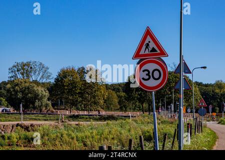 Verkehrszeichen mit Angabe: Maximale Geschwindigkeit 30 und Männer arbeiten, Arbeitszone im Straßenbau und -Reparatur, niederländische Landschaft mit Bäumen im Hintergrund, sunn Stockfoto