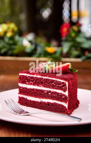 Ein Stück roter Samtkuchen, dekoriert mit frischer Erdbeere und Heidelbeere auf rosa Teller im Café im Freien. Stockfoto