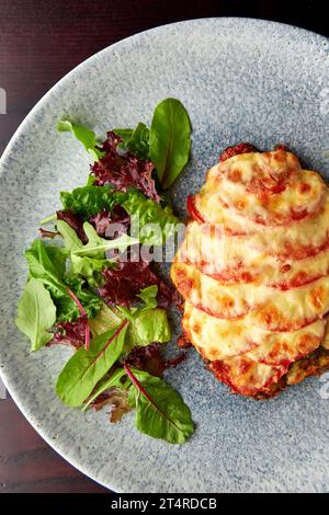 Leckerer Schweinekotelofen, gebacken mit Tomaten und Käse, serviert auf grauer Platte mit frischem Gemüse. Stockfoto