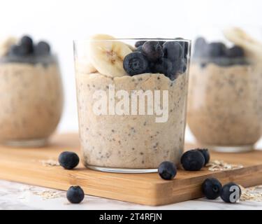 Ein gesundes Frühstück mit über Nacht Hafer auf einem hölzernen Schneidebrett und weißem Hintergrund. Garniert mit Banane und Heidelbeeren Stockfoto
