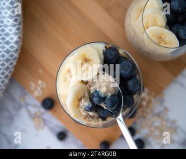 Ein gesundes Frühstück mit über Nacht Hafer auf einem hölzernen Schneidebrett und weißem Hintergrund. Garniert mit Banane und Heidelbeeren Stockfoto
