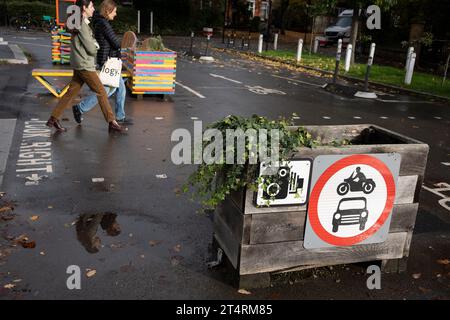 Fußgänger passieren Pflanzbarrieren, die eine LTN (Low Traffic Neighbourhood) bilden, eine Straßensperrung durch den Southwark Council, die Autofahrer daran hindert, die Kreuzung von Carlton Avenue und Dulwich Village zu erreichen. Einschränkungen verhindern auch, dass der Verkehr am 1. November 2023 in London in der Hauptverkehrszeit am Vormittag und Nachmittag durchfährt. Stockfoto