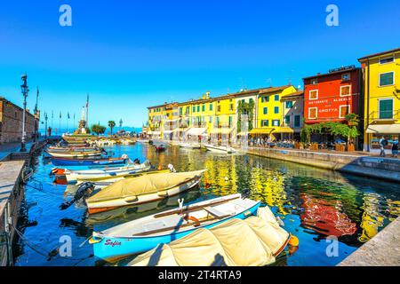 LAZISE, VENETO - ITALIEN - 28. SEPTEMBER 2018: Boote im alten Hafen von Lazise und Touristen, die morgens spazieren gehen. Die Stadt ist ein beliebtes Urlaubsziel Stockfoto