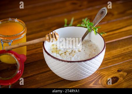 Haferbrei mit Honig zum Frühstück in einer Schüssel auf einem Holztisch. Stockfoto