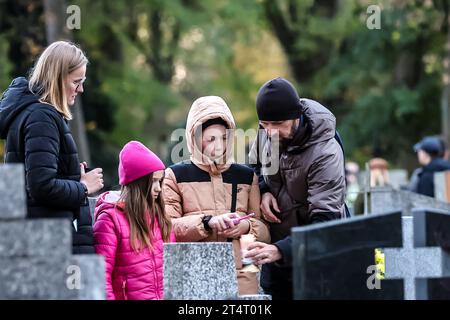 Krakau, Polen. November 2023. Eine Familie zündet am 1. November 2023 auf dem Rakowicki-Friedhof in Krakau, Polen, eine Kerze an. Allerheiligen in Polen ist ein sehr traditioneller Familienurlaub. Menschenmassen besuchen Friedhöfe im ganzen Land, um Kerzen anzuzünden und Blumen für die Verstorbenen zu bringen. (Foto: Dominika Zarzycka/SIPA USA) Credit: SIPA USA/Alamy Live News Stockfoto