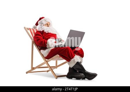 Santa claus und sitzt auf einem Liegestuhl und benutzt einen Laptop-Computer isoliert auf weißem Hintergrund Stockfoto