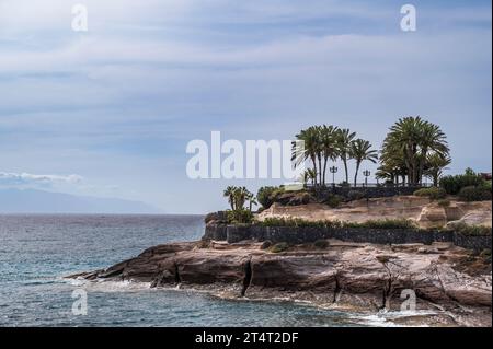 Spektakuläre Küste von Costa Adeja, Teneriffa. Der atlantik stürzt gegen die felsige Landzunge, wo exotische Palmen zu sehen sind. Stockfoto