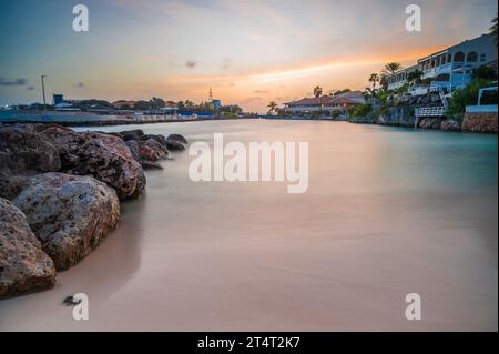 Ein kleiner Karibikstrand, bei Sonnenuntergang. Das Meer wird durch eine lange Verschlusszeit geglättet. Private Häuser mit Blick auf den Strand Stockfoto