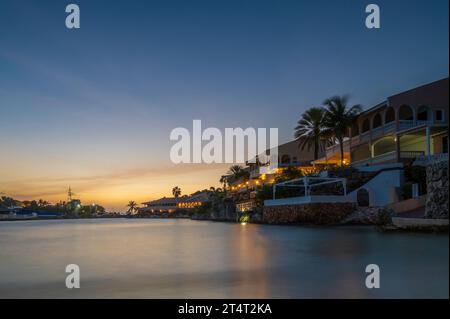 Ein kleiner Karibikstrand, bei Sonnenuntergang. Das Meer wird durch eine lange Verschlusszeit geglättet. Private Häuser mit Blick auf den Strand Stockfoto