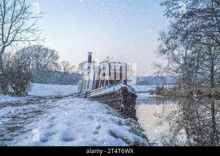 Das britische Schmalboot, das auf einem Kanal von Worcestershire an einem verschneiten Ufer und einem Schleppweg mit Schnee auf dem Boden und Schneefall vertäut ist. Stockfoto