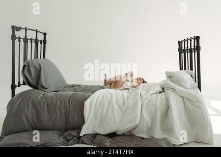 Porträt eines auf dem Bett liegenden Kindes und Trinkwasser aus einer Flasche. Familienkonzept. Blick durch die Metallstangen des Bettes. Stockfoto