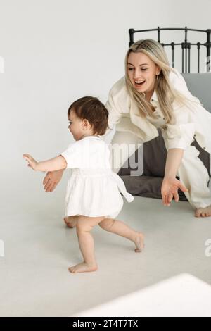 Mom spielt mit ihrer Tochter, holt sie im Zimmer ein, versucht sie zu fangen, lächelt. Zeit Entspannen. Eine glückliche Familie. Stockfoto