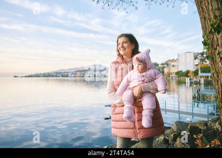 Außenporträt einer glücklichen jungen Mutter mit entzückendem Mädchen, das einen schönen Blick auf den Wintersee Genf oder Lac Leman, Montreux, Schweiz genießt Stockfoto