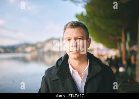 Außenporträt eines hübschen 40-jährigen Mannes mit schwarzem Mantel Stockfoto