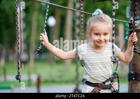 Niedliches Mädchen, das Aktivitäten in einem Kletterpark genießt. Das Mädchen geht auf die Scharnierspur. Stockfoto