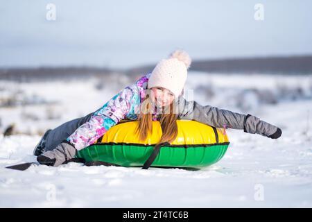 Das junge Mädchen streckte ihre Arme aus, während es bei sonnigem Winterwetter Snowtubing genoss Stockfoto